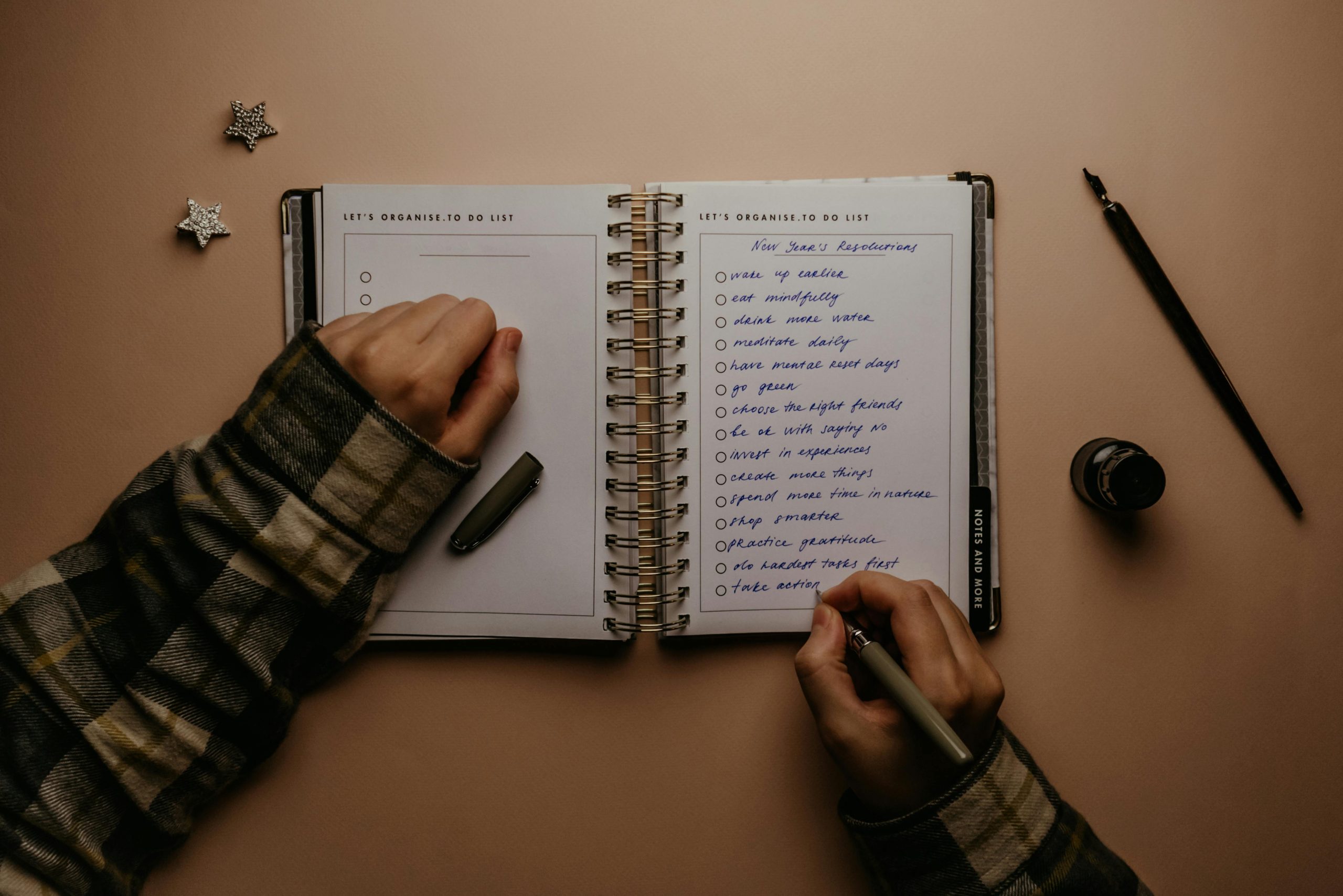 Overhead shot of a person writing New Year's resolutions in a notebook on a desk.